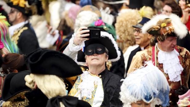 Ein Mann mit Maske und historischem Kostüm macht ein Foto mit seinem Smartphone.
