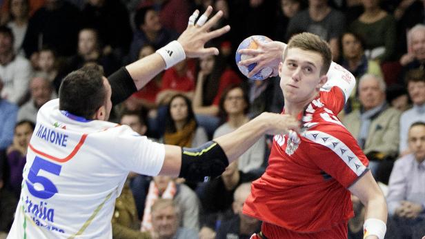 Ein Handballspieler im roten Trikot wirft den Ball, während ein Gegenspieler ihn zu blocken versucht.