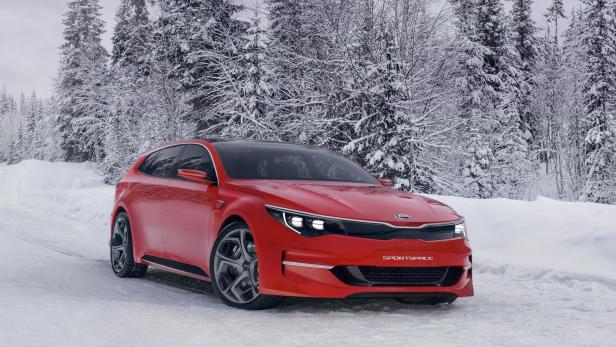 Ein roter Kia Sportspace steht im Schnee vor einem verschneiten Wald.