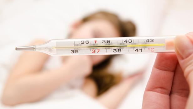 Ein Thermometer zeigt eine erhöhte Temperatur bei einem Kind im Hintergrund.