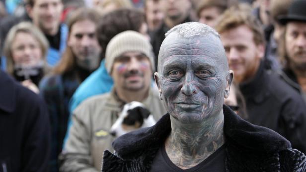 Ein Mann mit Gesichtstattoos steht vor einer Menschenmenge.