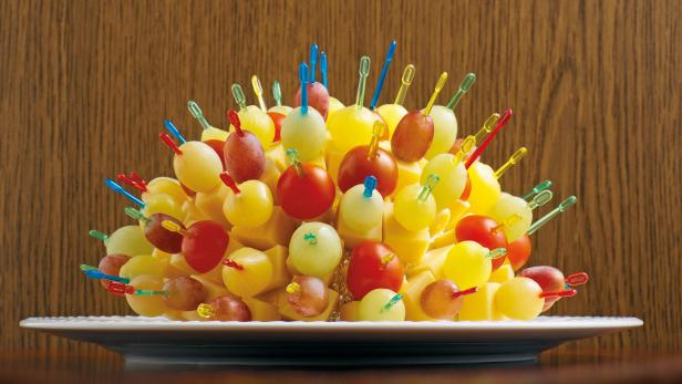 Ein Käseigel mit Käsewürfeln, Tomaten und Weintrauben auf einem Teller.