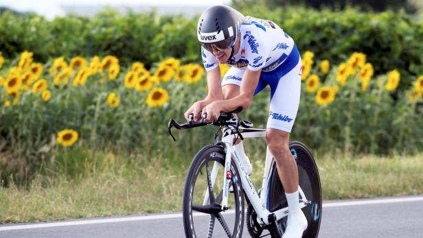 Ein Radfahrer fährt auf einer Straße an einem Feld mit Sonnenblumen vorbei.