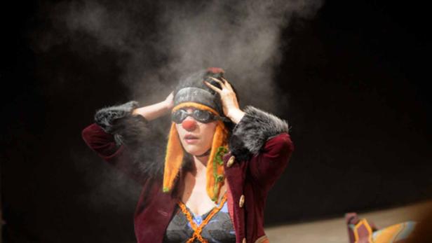 Eine Person mit Clown-Make-up und Brille steht im Rampenlicht.