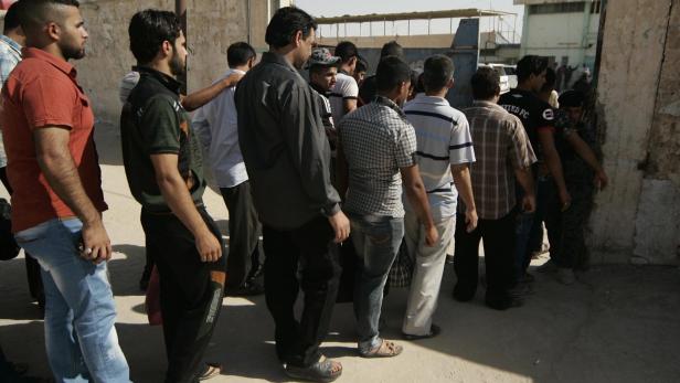 Eine Menschenmenge steht an einer staubigen Straße an einer Wand Schlange.