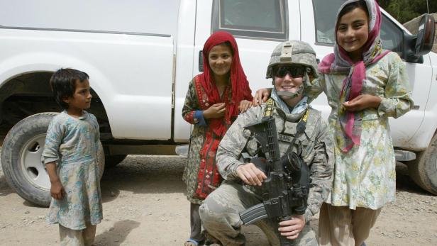 Eine US-Soldatin kniet mit drei afghanischen Mädchen vor einem weißen Militärfahrzeug.