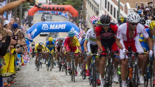 Eine Gruppe Radfahrer fährt ein Kopfsteinpflaster hinauf, angefeuert von Zuschauern.