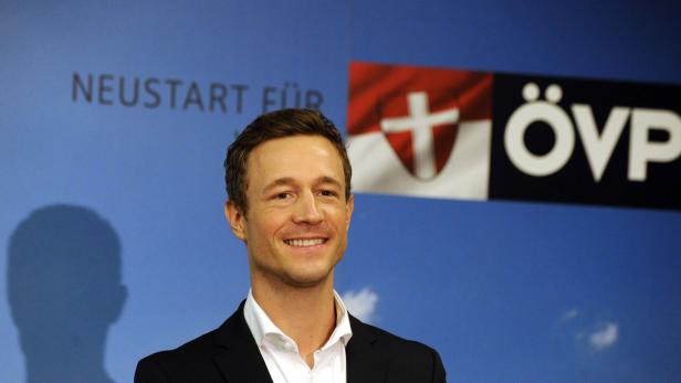 Ein lächelnder Mann vor einem Hintergrund mit dem ÖVP-Logo.