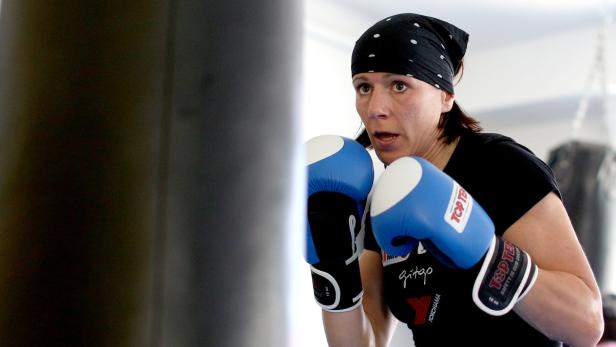 Eine Frau mit Boxhandschuhen trainiert mit einem Sandsack.