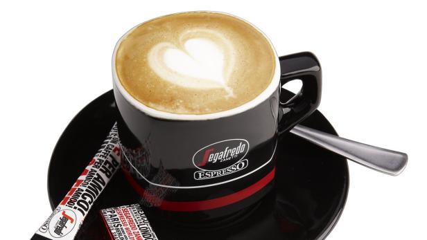 Eine Tasse Cappuccino mit Herzmuster im Milchschaum steht auf einer Untertasse.