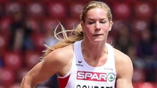 Eine blonde Athletin in einem weißen Trikot läuft auf einer roten Laufbahn.