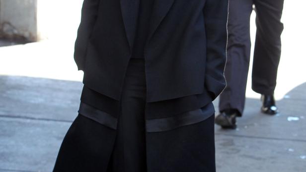 Victoria Beckham in einem schwarzen Mantel und zweifarbigen Schuhen auf der Straße.