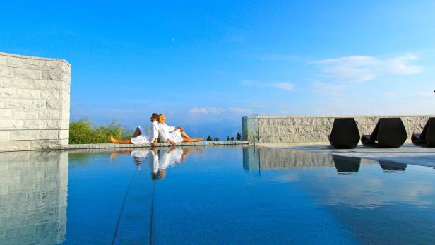 Ein Paar in Bademänteln entspannt am Rand eines Pools mit Blick auf die Landschaft.