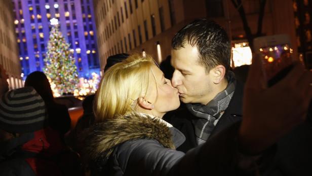 Ein Paar küsst sich vor einem Weihnachtsbaum in der Stadt.