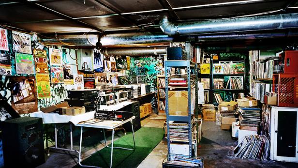 Ein Raum voller Schallplatten, Musikanlagen und Postern an den Wänden.