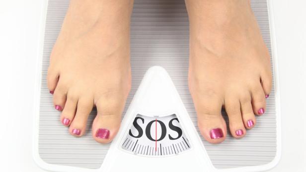 Füße mit lackierten Zehennägeln stehen auf einer Waage, die „SOS“ anzeigt.