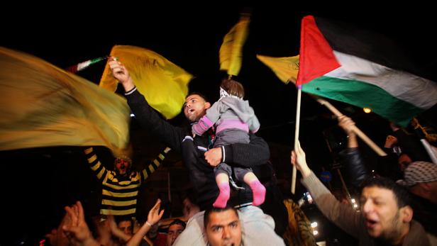 Männer mit palästinensischen und gelben Flaggen feiern mit einem Kind auf den Schultern.