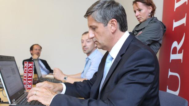 Ein Mann im Anzug tippt auf einem Laptop, während andere Personen im Hintergrund sitzen.