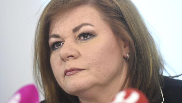 Eine Frau mit braunen Haaren und dunklem Make-up blickt nach links.