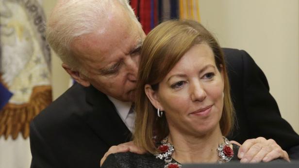 Joe Biden flüstert einer Frau mit einer auffälligen Halskette etwas ins Ohr.