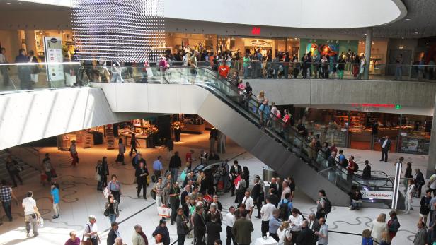 Viele Menschen in einem belebten Einkaufszentrum mit Rolltreppen.