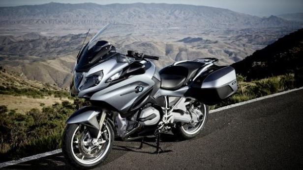 Ein silbernes BMW-Motorrad steht auf einer asphaltierten Straße mit Bergen im Hintergrund.