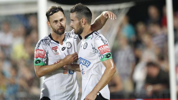 Zwei Fußballspieler in weißen Trikots umarmen sich auf dem Spielfeld.