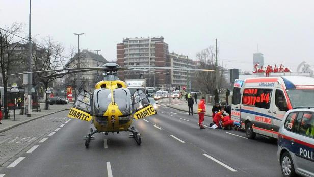 Ein gelber ÖAMTC-Rettungshubschrauber steht auf einer Straße in Wien neben einem Rettungswagen.
