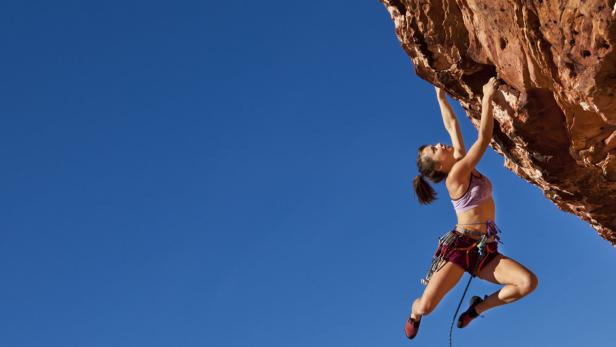 Female rock climber struggles up a cliff for her next grip on a challenging ascent.