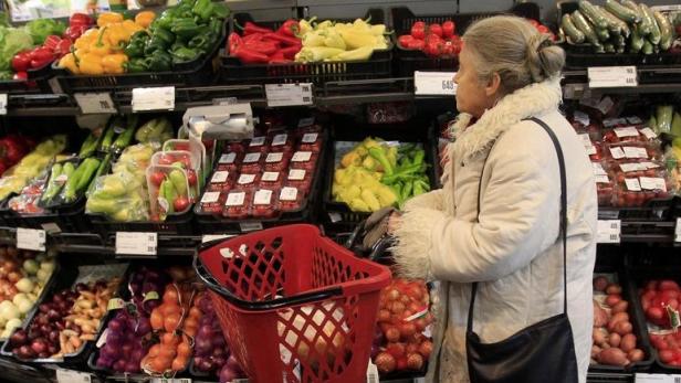 Eine Frau mit einem roten Einkaufskorb wählt Gemüse in einem Supermarkt aus.