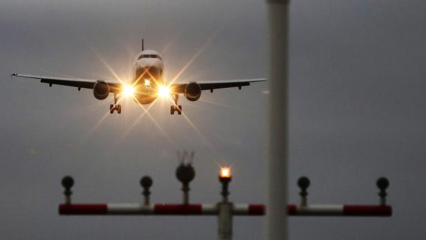 Ein Flugzeug landet mit eingeschalteten Scheinwerfern auf einer Landebahn.