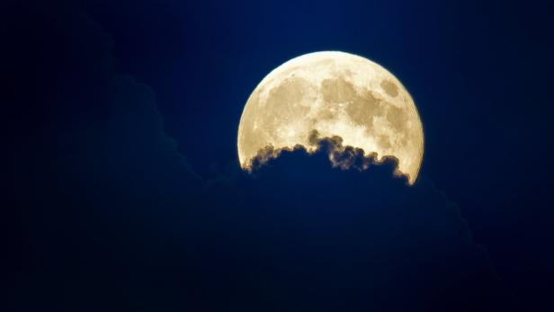 Ein fast voller Mond scheint hinter dunklen Wolken.