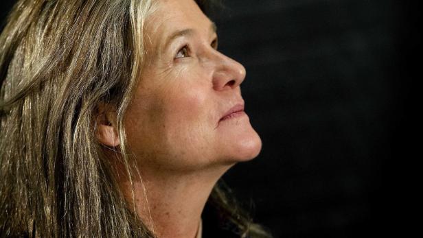 Eine Frau mit langen, graumelierten Haaren blickt nach oben.