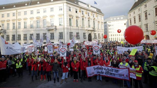 Eine Demonstration mit vielen Menschen und roten Luftballons vor einem Gebäude in Wien.