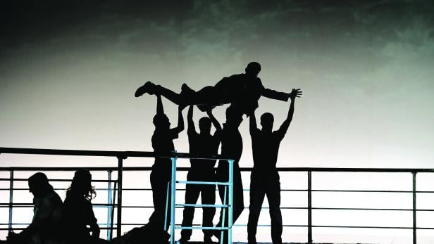 Eine Gruppe von Personen hebt eine andere Person in die Luft, alle als Silhouetten dargestellt.