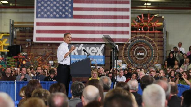 Barack Obama spricht vor einer Menschenmenge vor einer großen US-Flagge.