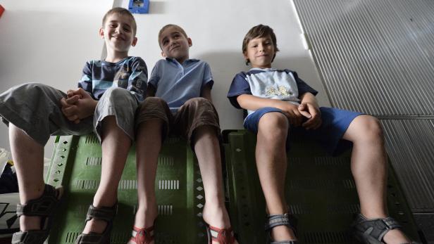 Drei Jungen sitzen auf grünen Kisten und schauen in die Kamera.