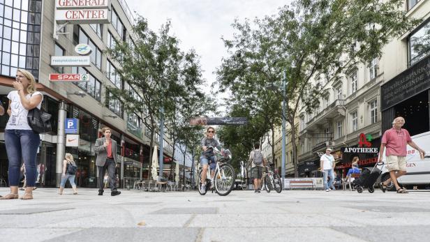 Eine belebte Straße in Wien mit Fußgängern und einer Radfahrerin.