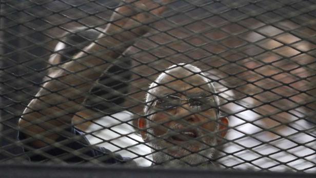 Ein Mann mit Brille und Bart hinter einem Gitter.