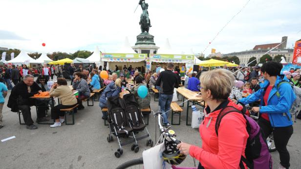 Menschen sitzen an Tischen auf dem Rathausplatz in Wien.