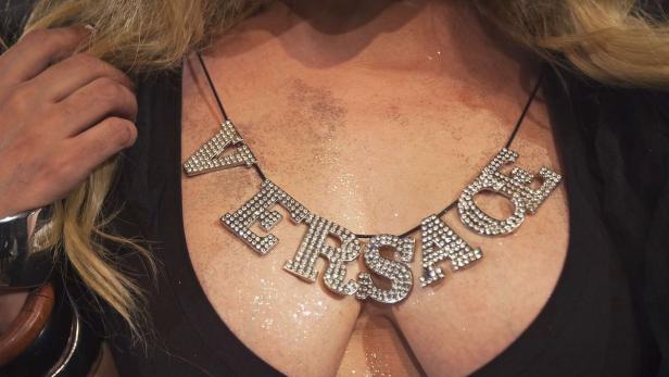 Eine Person trägt eine glitzernde „Versace“-Halskette.