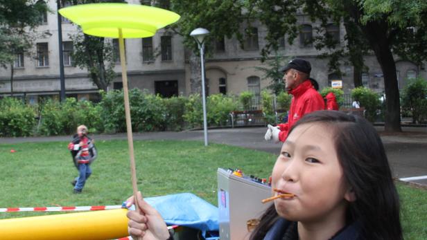 Ein Mädchen balanciert einen Teller auf einem Stab und isst dabei eine Salzstange.