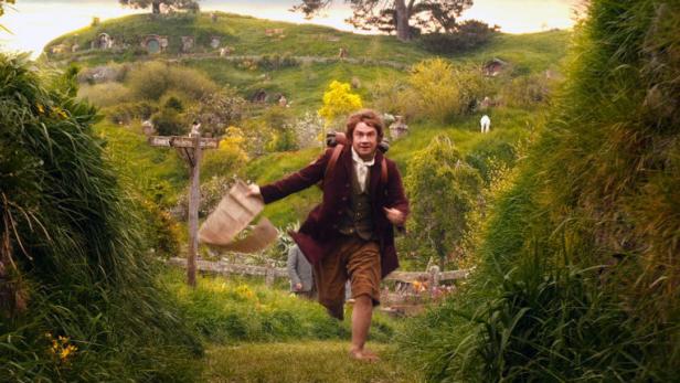 Ein Hobbit rennt barfuß mit einem Brief durch das Auenland.