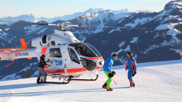 Ein Notarzthubschrauber steht vor einer verschneiten Bergkulisse.