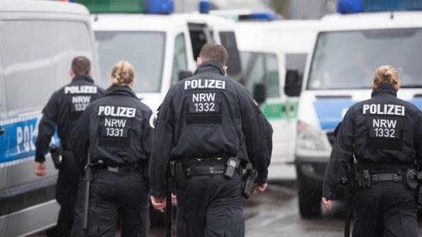 Mehrere Polizisten der NRW-Polizei stehen vor ihren Einsatzfahrzeugen.