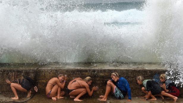Eine Gruppe von Menschen kauert sich vor einer großen Welle, um sich vor dem Spritzwasser zu schützen.