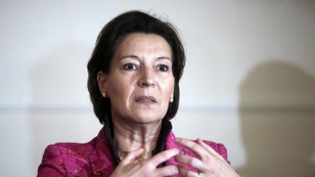 Eine Frau mit dunklen Haaren und einem pinkfarbenen Blazer gestikuliert.