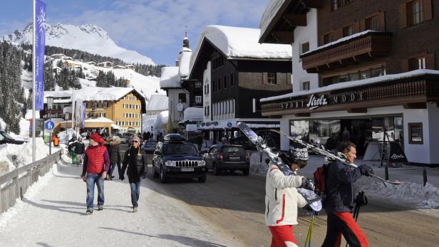 Menschen gehen in einem verschneiten Skiort an Geschäften und Hotels vorbei.
