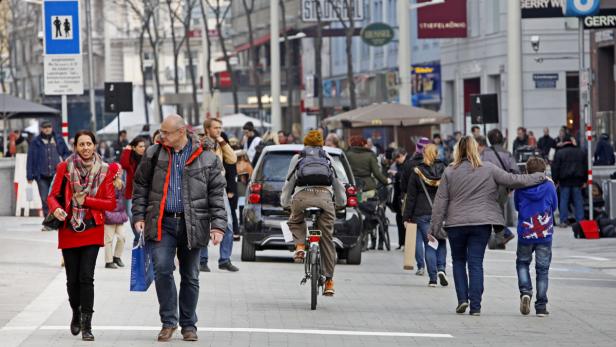 Menschen gehen und fahren Fahrrad auf einer belebten Straße in der Stadt.