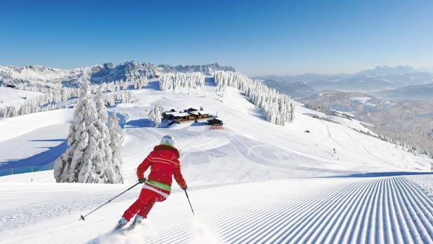 Eine Skifahrerin fährt eine präparierte Piste in einem verschneiten Skigebiet hinunter.